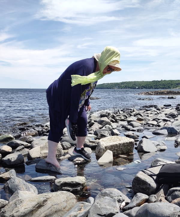 Woman in sun hat dipping her toe into the shore waters of the Atlantic Ocean.